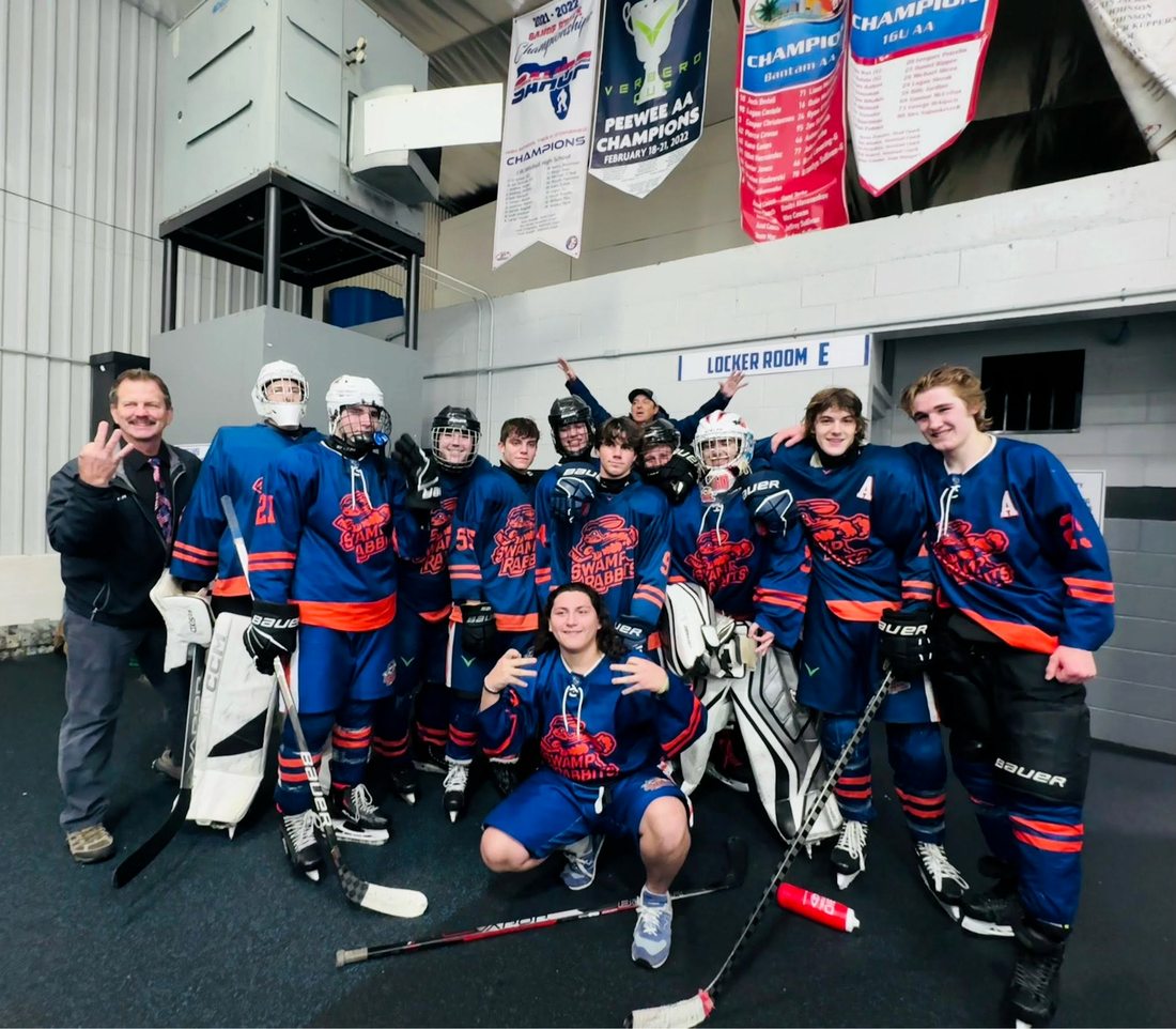 Coach Zerkle’s DME Swamp Rabbits team in blue and orange jerseys, posing outside Locker Room E under championship banners